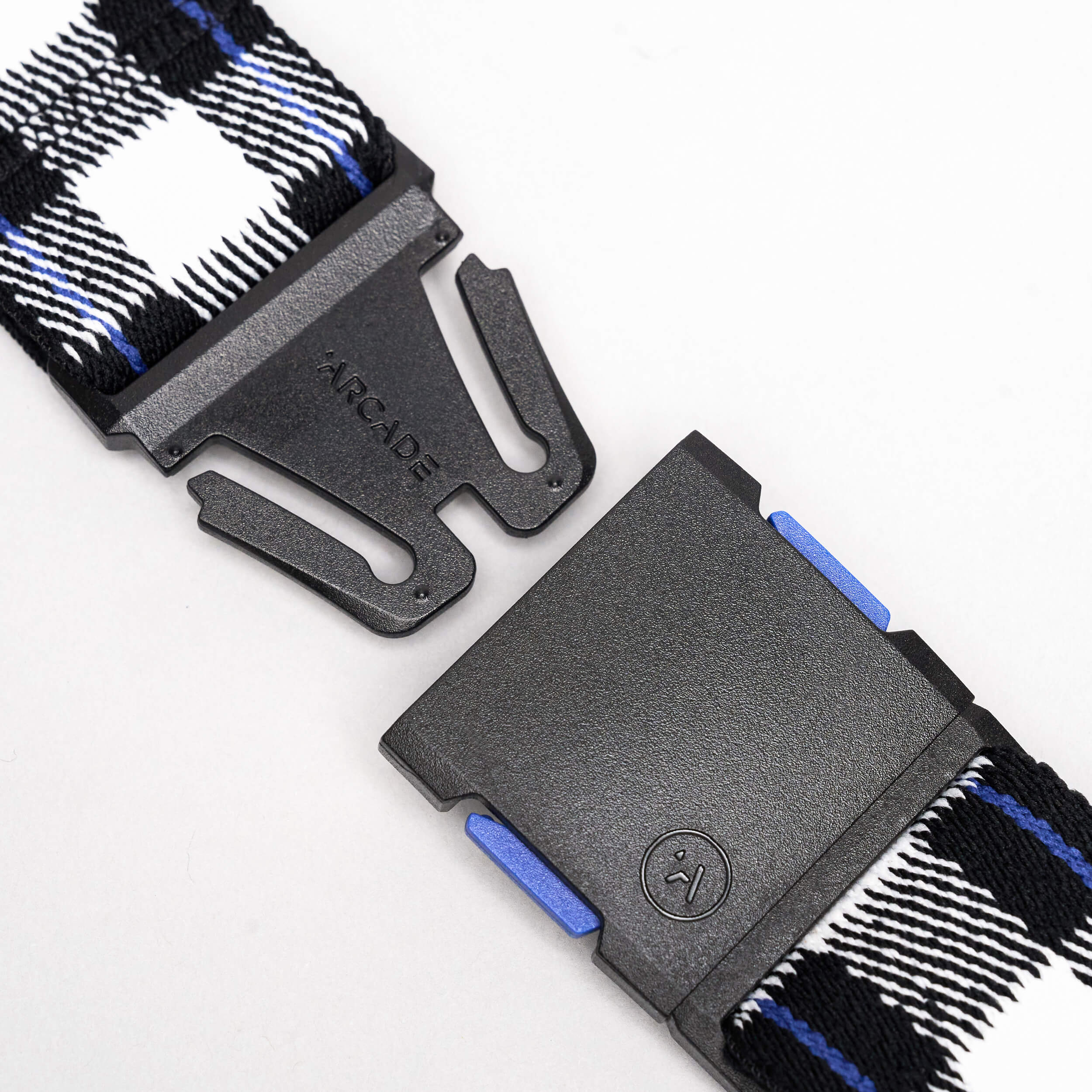 Close-up of the Arcade Belts Plaid: a low-profile black buckle with Arcade branding, attached to a black, white, and blue plaid woven strap. Shown unclasped against a white background—ideal for travel.