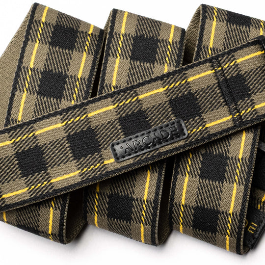 A close-up of the Plaid belt by Arcade Belts in olive green, black, and yellow with a black ARCADE logo patch. Displayed in overlapping folds on a white background, this limited-edition style features new colors.