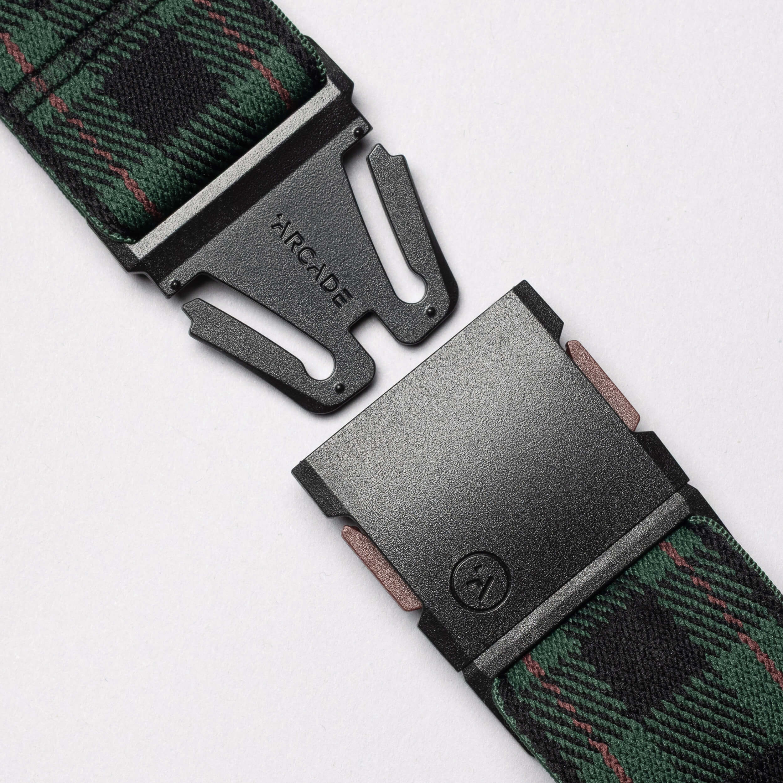 Close-up of the Plaid Elastic Stretch Belt by Arcade Belts, featuring a green and black plaid pattern and a black ARCADE-labeled metal buckle, shown partially unbuckled on a light background.