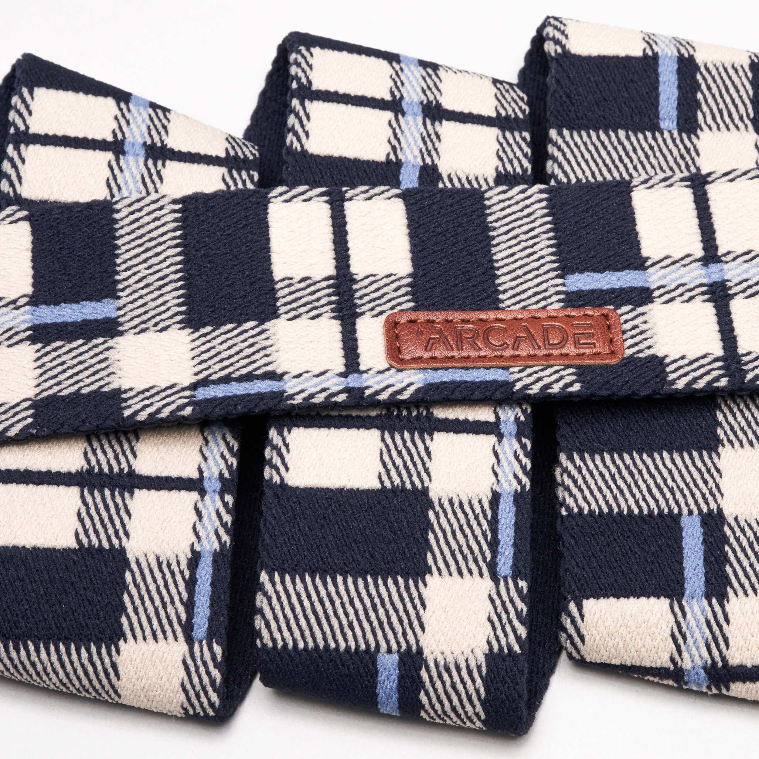 Plaid by Arcade Belts: a navy, cream, and light blue plaid elastic stretch belt with a brown leather patch embossed ARCADE—offering style and comfort anywhere.