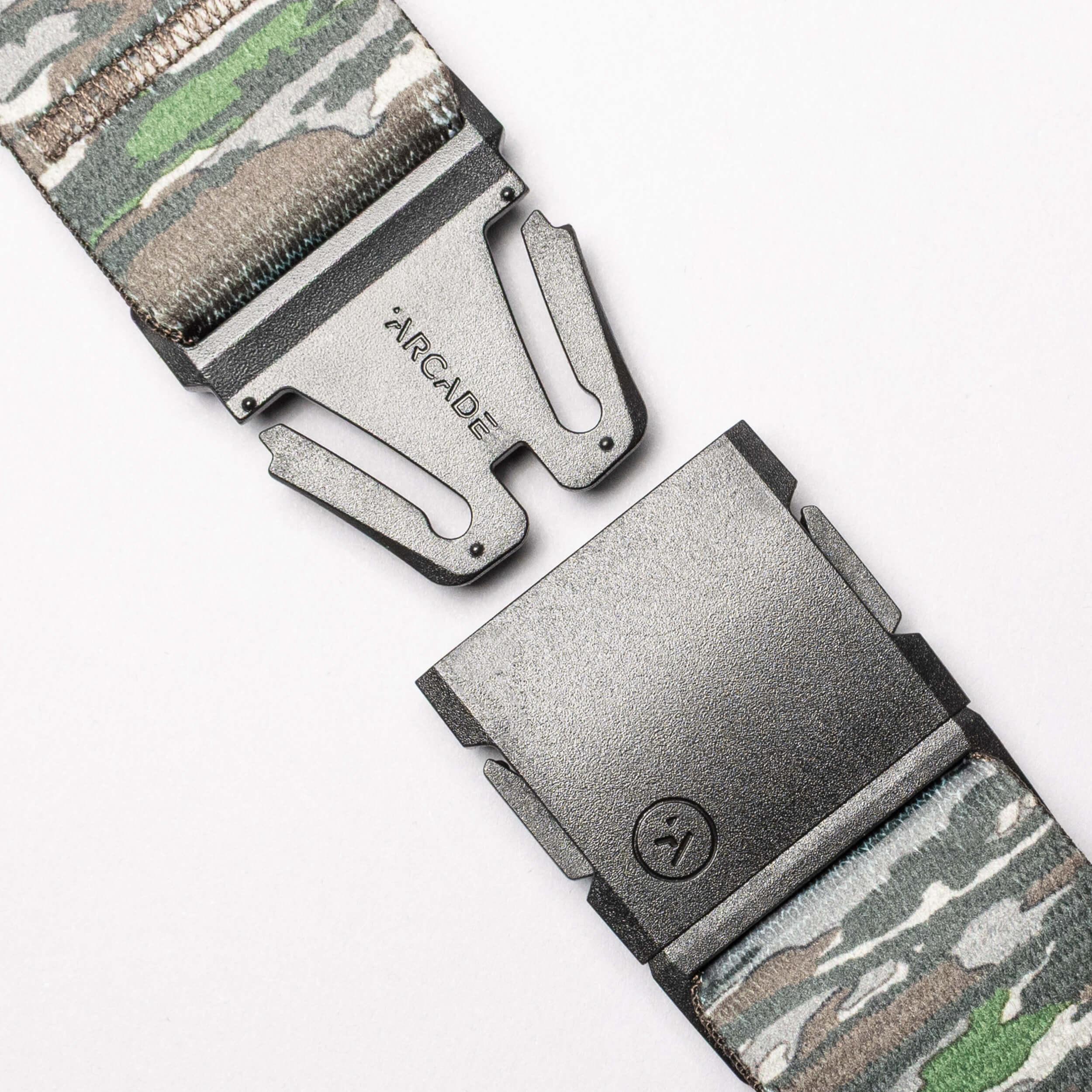 Close-up of the Realtree Camo Original by Arcade Belts, a stretch webbing belt with a camouflage pattern, partially open metal buckle engraved “ARCADE,” and a small lower logo.