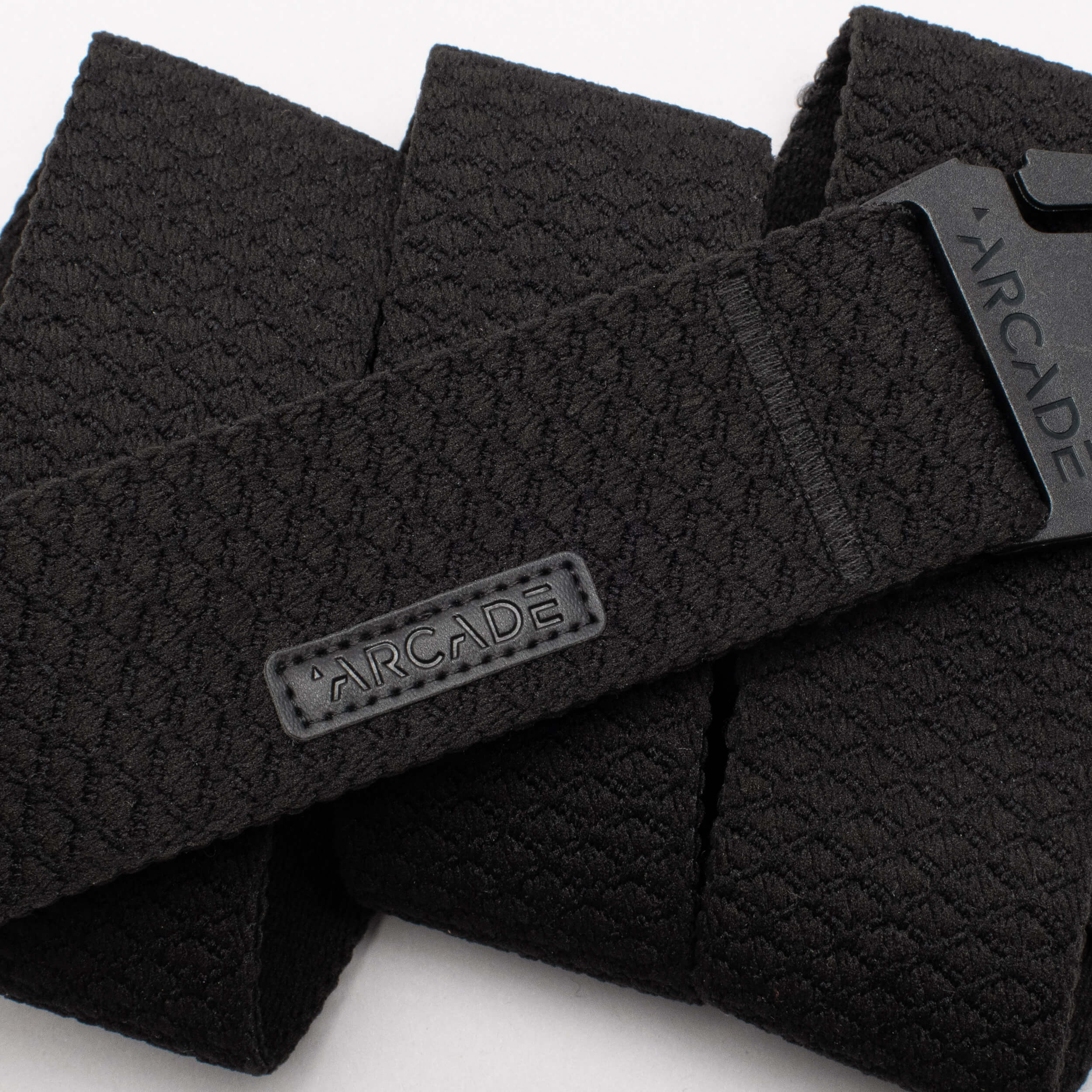 A close-up of the Salient belt by Arcade Belts, featuring black textured material, a rectangular ARCADE fabric label, and a plastic buckle engraved with ARCADE—ideal for those seeking reliable travel belts.