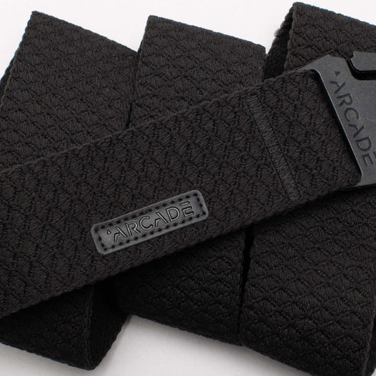 A close-up of the Salient belt by Arcade Belts, featuring black textured material, a rectangular ARCADE fabric label, and a plastic buckle engraved with ARCADE—ideal for those seeking reliable travel belts.