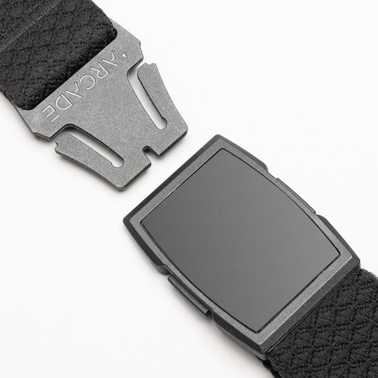 Close-up of the Salient belt by Arcade Belts, featuring an elastic strap, matte black rectangular buckle, and a notched metal clasp engraved with ARCYDE. Buckle and clasp are separated on a light background to showcase its modern design.