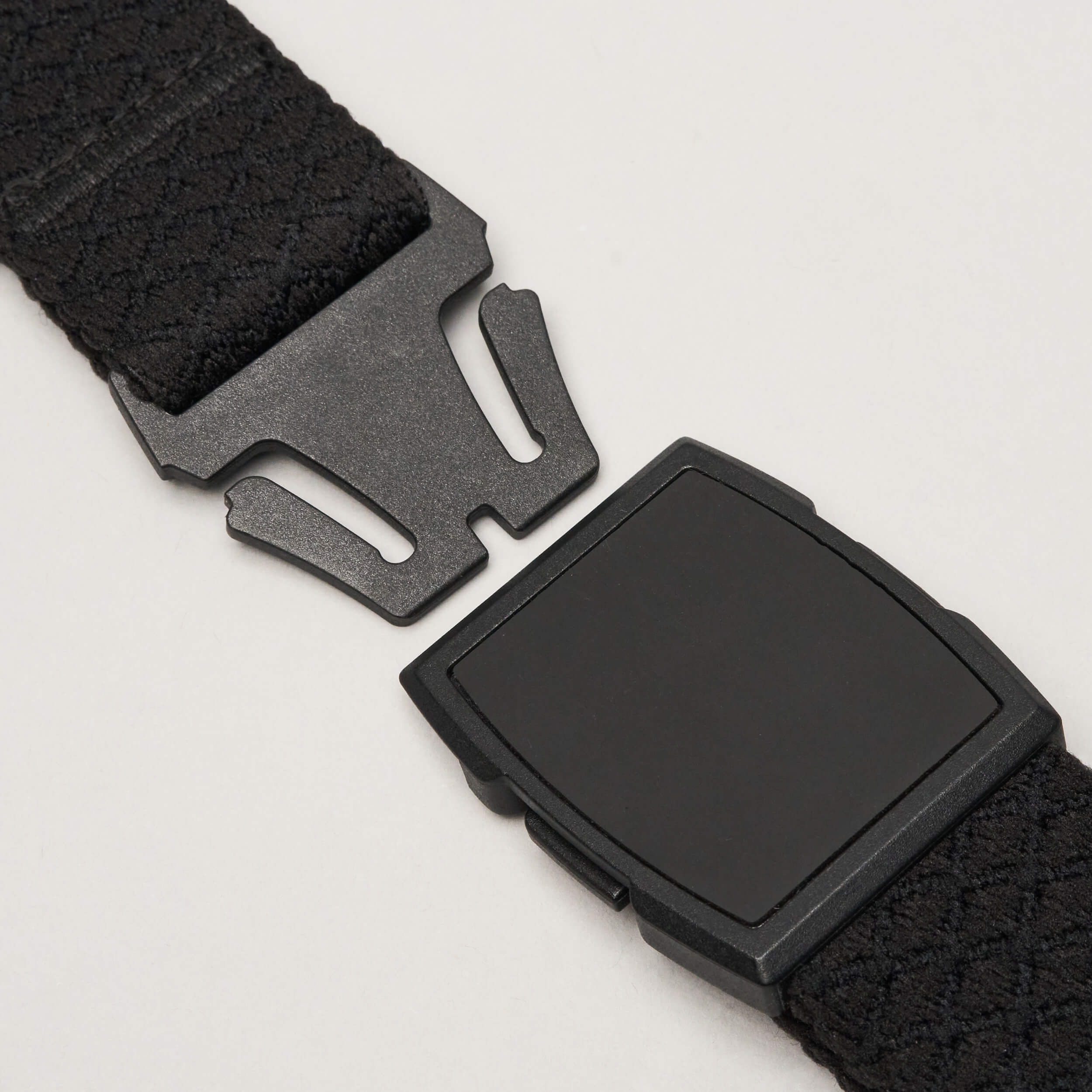 Close-up of the Arcade Belts Salient: a black fabric strap with a rectangular plastic buckle and prong connector, shown open against a light gray background to display its travel belt mechanism.