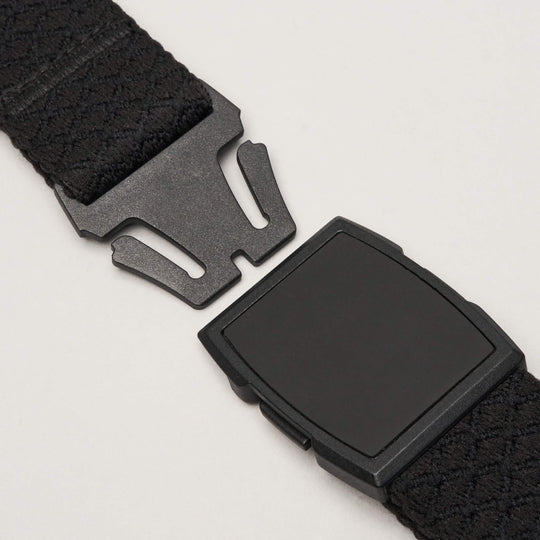 Close-up of the Arcade Belts Salient: a black fabric strap with a rectangular plastic buckle and prong connector, shown open against a light gray background to display its travel belt mechanism.