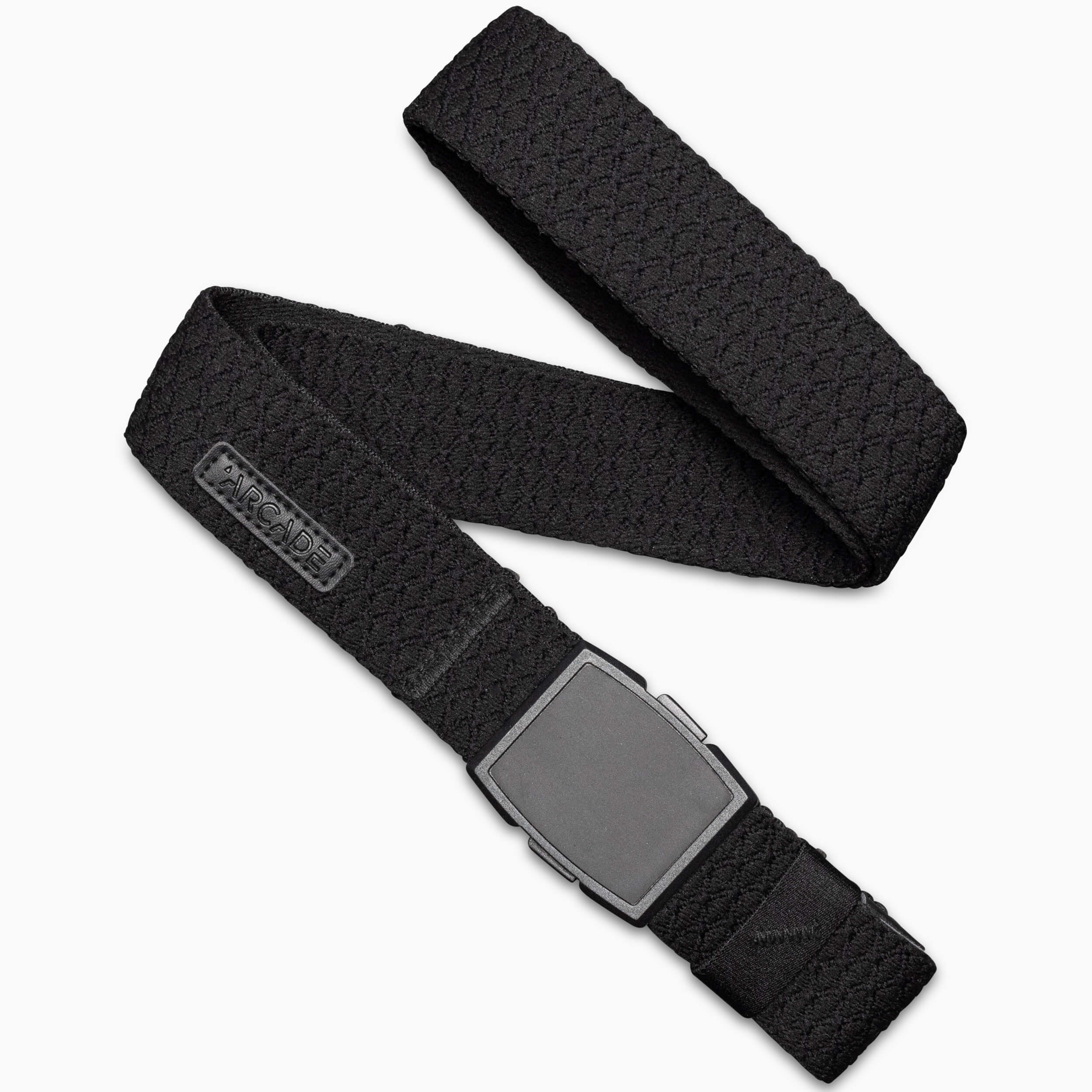 The Salient by Arcade Belts is a black woven belt with a flat, rectangular matte black plastic buckle, coiled on a white background. A small brand logo tag appears near the buckle.