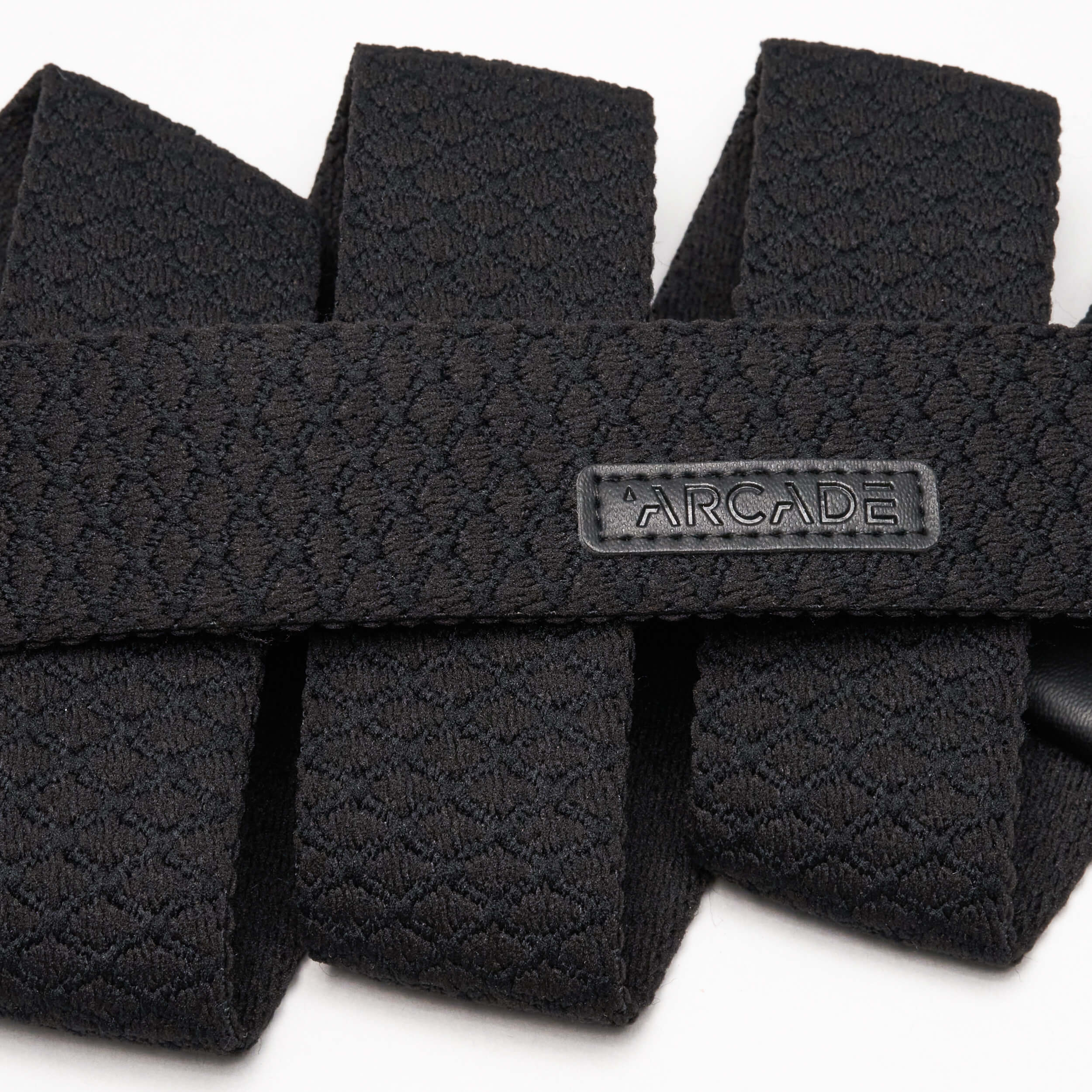 Close-up of the Salient, a textured black stretch webbing belt by Arcade Belts, featuring a rectangular rubber ARCADE label. The neatly folded belt showcases its detailed pattern, flexible durability—perfect for enthusiasts and travelers alike.