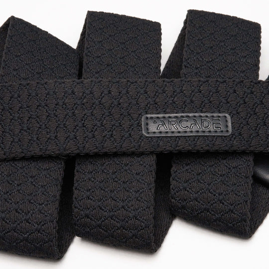 Close-up of the Salient, a textured black stretch webbing belt by Arcade Belts, featuring a rectangular rubber ARCADE label. The neatly folded belt showcases its detailed pattern, flexible durability—perfect for enthusiasts and travelers alike.