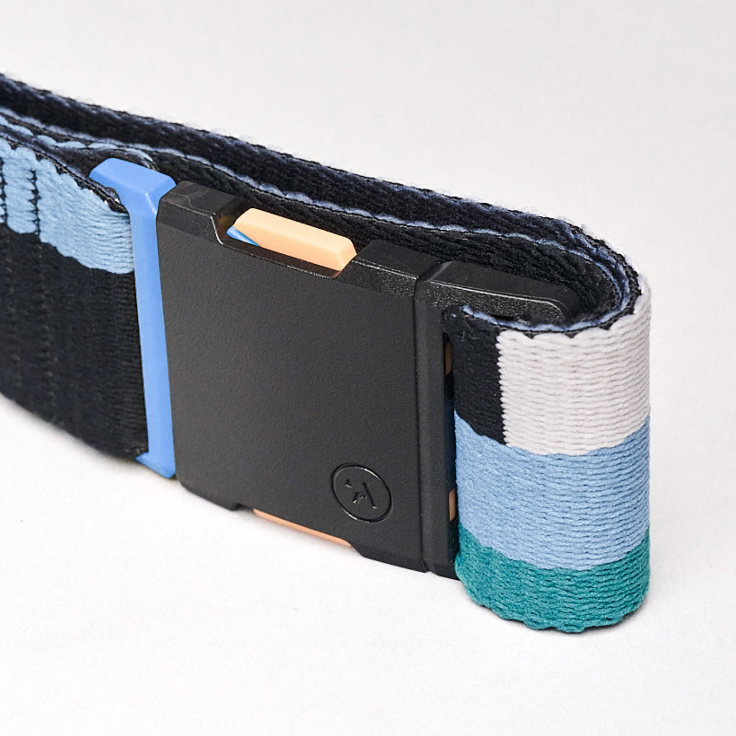 A close-up of the Arcade Belts Sierra, a low-profile belt with blue, white, black, and teal stretch webbing stripes. It has a black rectangular buckle and a small circular logo, shown coiled on a plain white background.