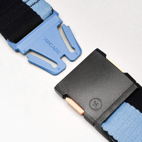 Close-up of the Sierra belt by Arcade Belts, featuring a blue and black adjustable strap with a plastic buckle. The blue section is labeled Arcade, while the black section has a textured button and beige release tabs.
