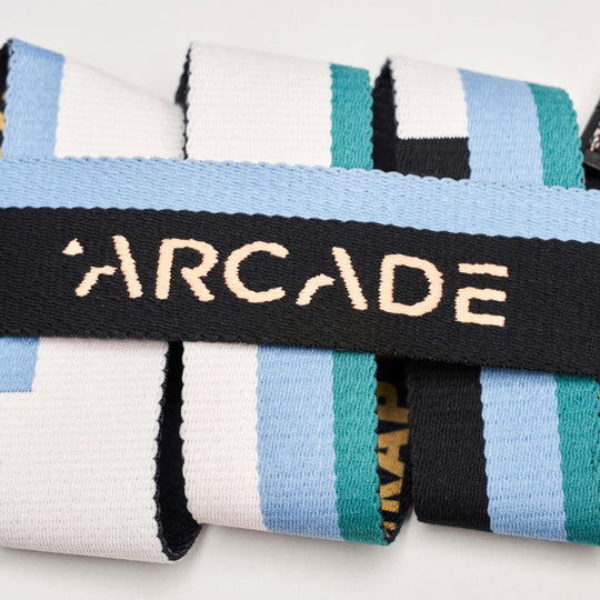 A close-up of the Arcade Belts Sierra features ARCADE stitched in beige letters on black, with blue, green, white, and black stripes, highlighting its low-profile belt design.