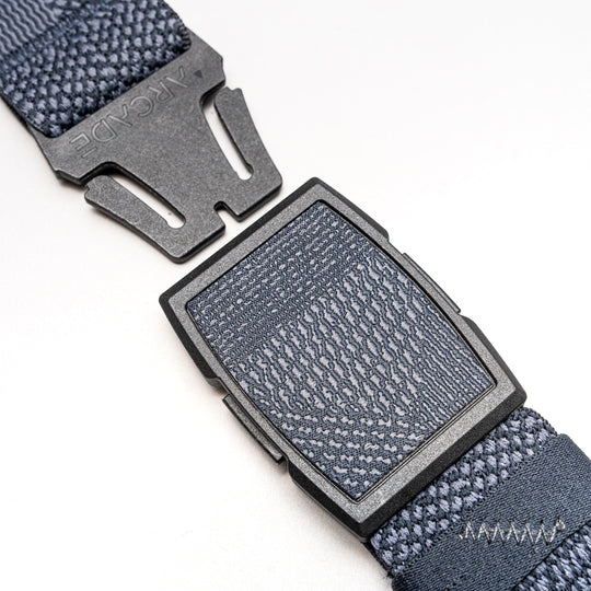 Close-up of the Skyline gray woven Elastic Stretch Belt by Arcade Belts, partially unclasped. The low-profile plastic buckle features a textured pattern with Arcade embossed on one side.