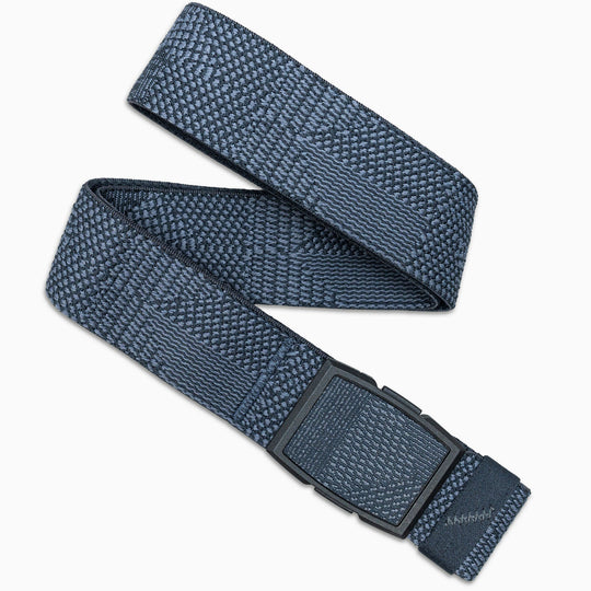 The Arcade Belts Skyline is a blue woven elastic stretch belt with a textured pattern and black rectangular buckle, shown loosely coiled against a white background with the buckle in the foreground.