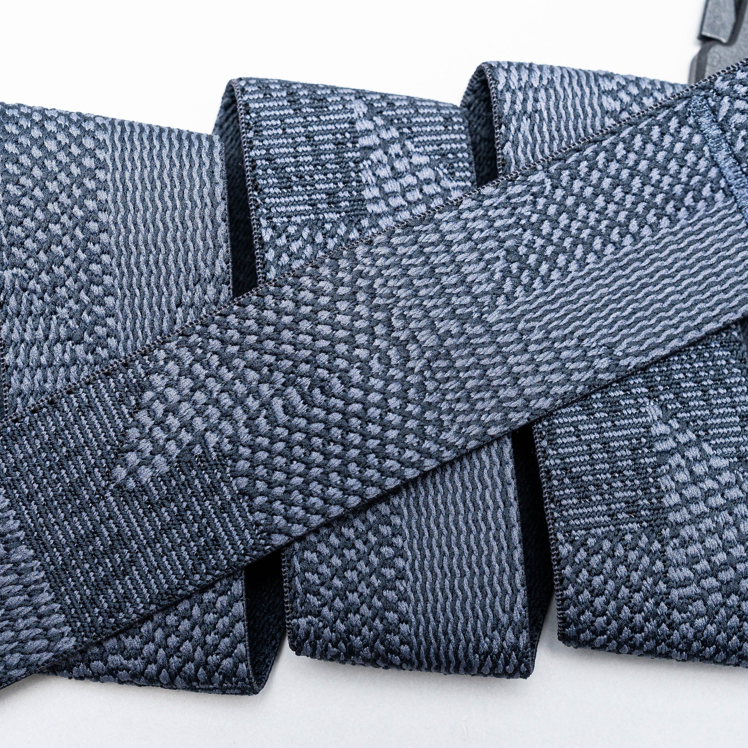 Close-up of several gray Skyline belts by Arcade Belts, featuring woven, textured webbing straps arranged in overlapping layers against a white background.
