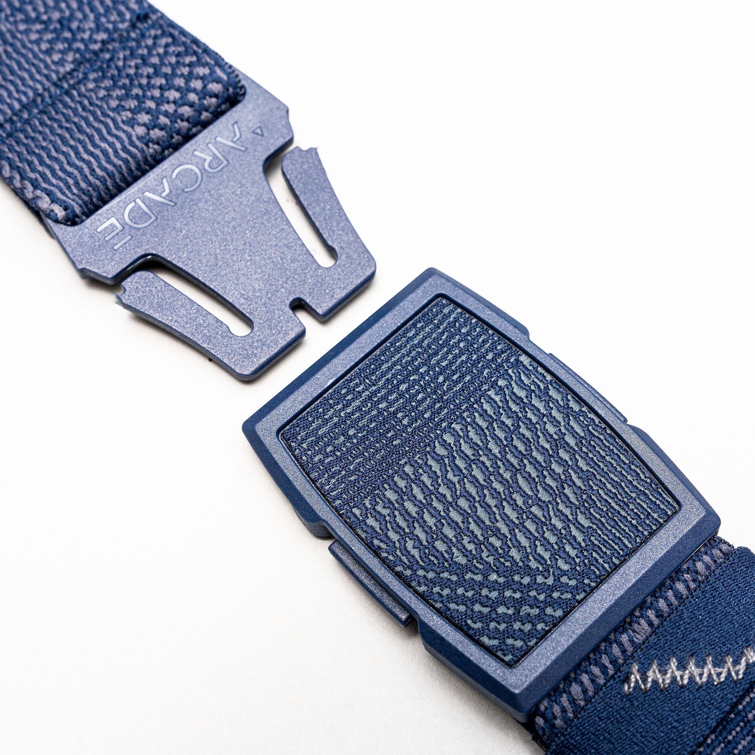 Close-up of the Arcade Belts Skyline, a blue stretch webbing belt with a plastic buckle engraved with “ARCADE,” shown on a plain white background.