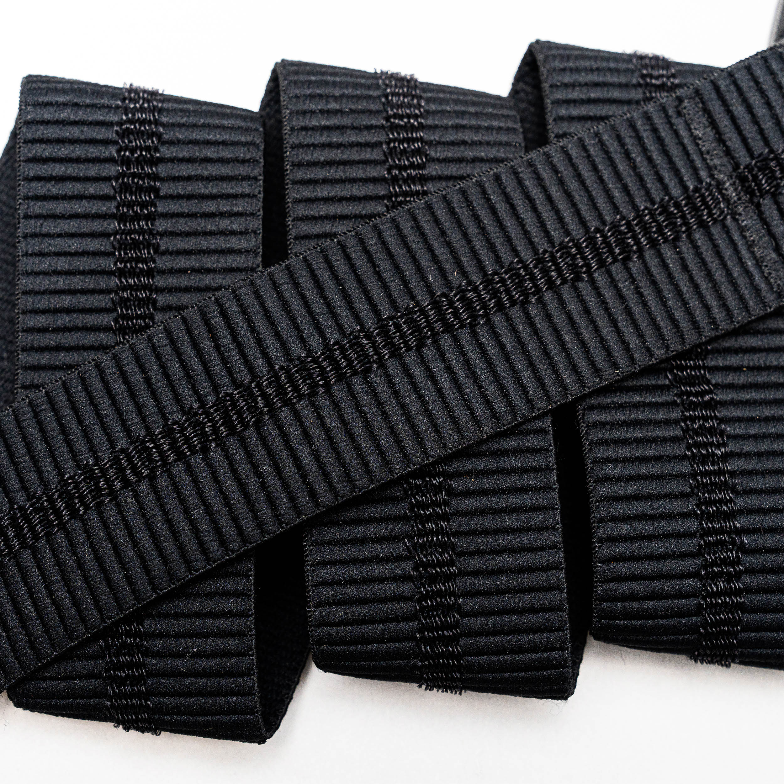 A close-up of the Arcade Belts Stamped black, ribbed elastic band with vertical stitching, neatly rolled on a white surface—perfect stretch webbing for low profile belt designs or use with a plastic buckle.