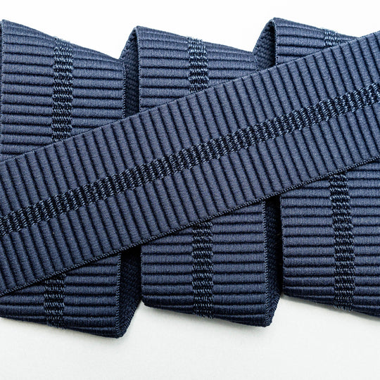 A close-up of three parallel navy blue Stamped stretch webbing ribbons from Arcade Belts, overlapped diagonally by a fourth ribbon with a similar pattern, all set against a white background.