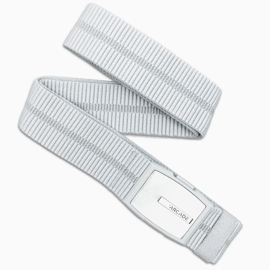 The Arcade Belts Stamped is a light gray elastic belt with vertical stripes and a rectangular silver buckle featuring the ARCADE logo, shown coiled loosely on a white background—perfect for travel.
