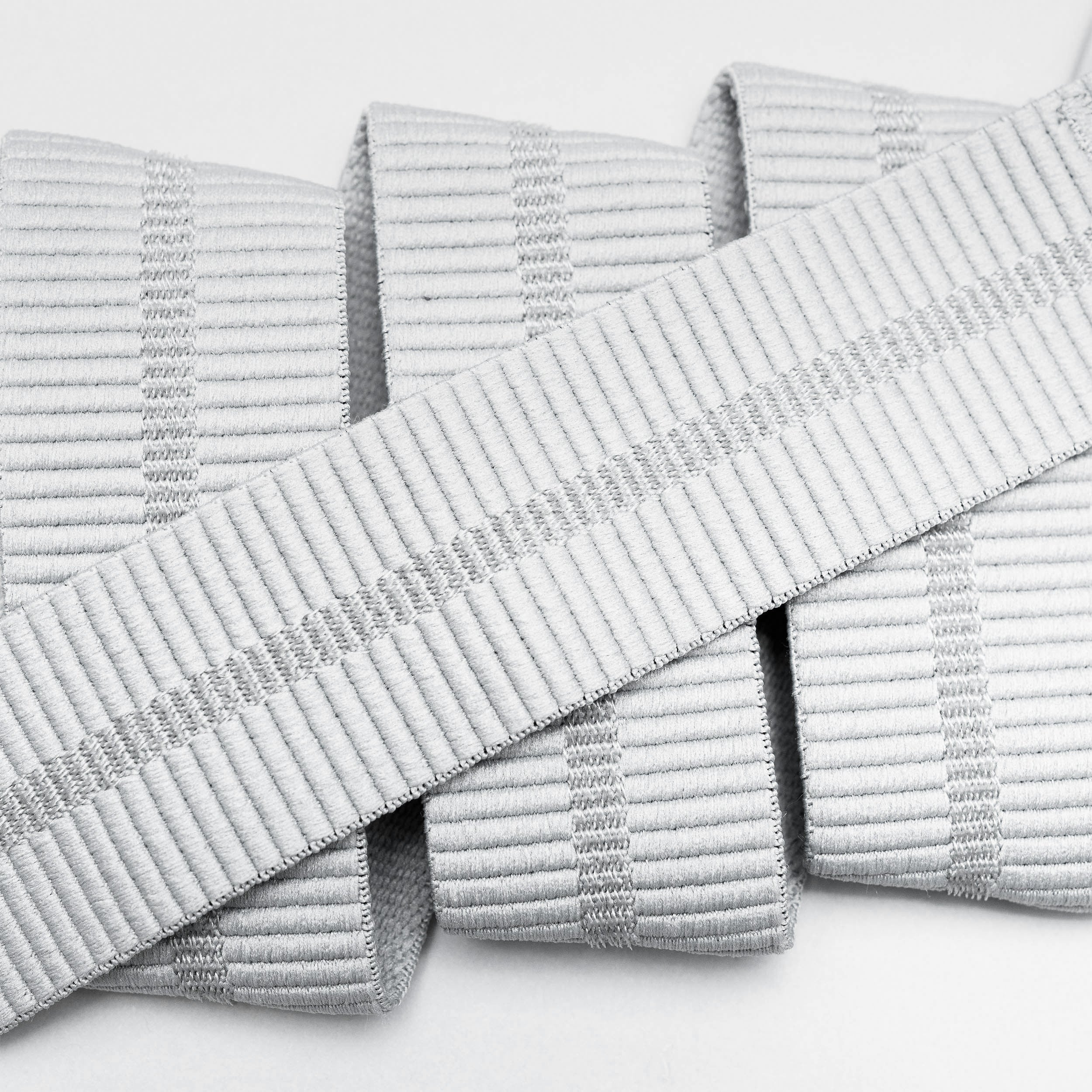 Close-up of Arcade Belts Stamped: white, textured ribbed fabric strips arranged parallel, with one laid diagonally. The material, resembling a low profile belt, features subtle vertical ridges and light grey stripe accents.