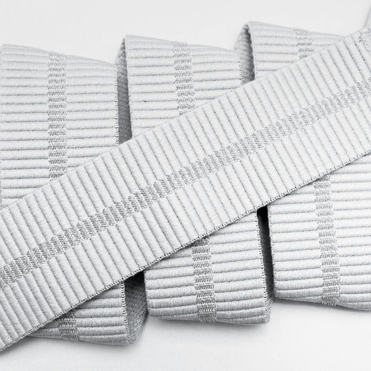 Close-up of Arcade Belts Stamped: white, textured ribbed fabric strips arranged parallel, with one laid diagonally. The material, resembling a low profile belt, features subtle vertical ridges and light grey stripe accents.
