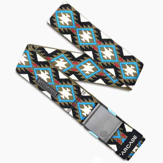 The Vernan Kee by Arcade Belts features stretch webbing with a blue, white, olive green, and black geometric diamond pattern, a grey rectangular buckle, and a black tag with ARCADE in white. Ideal for travel.
