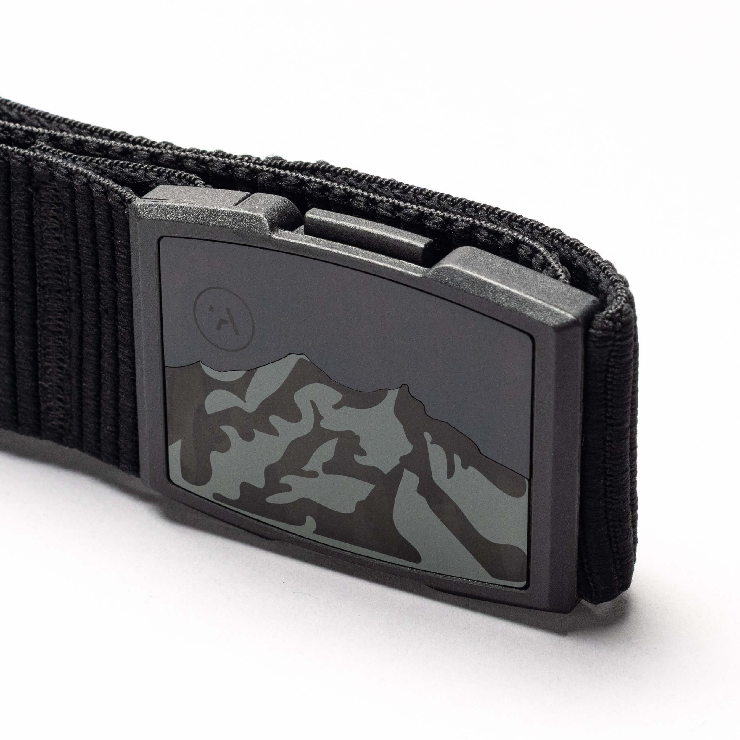 Close-up of the Arcade Belts Woody elastic stretch belt with a metal buckle featuring a mountain range design and an etched moon or sun in the corner. The white background highlights this low-profile belt.