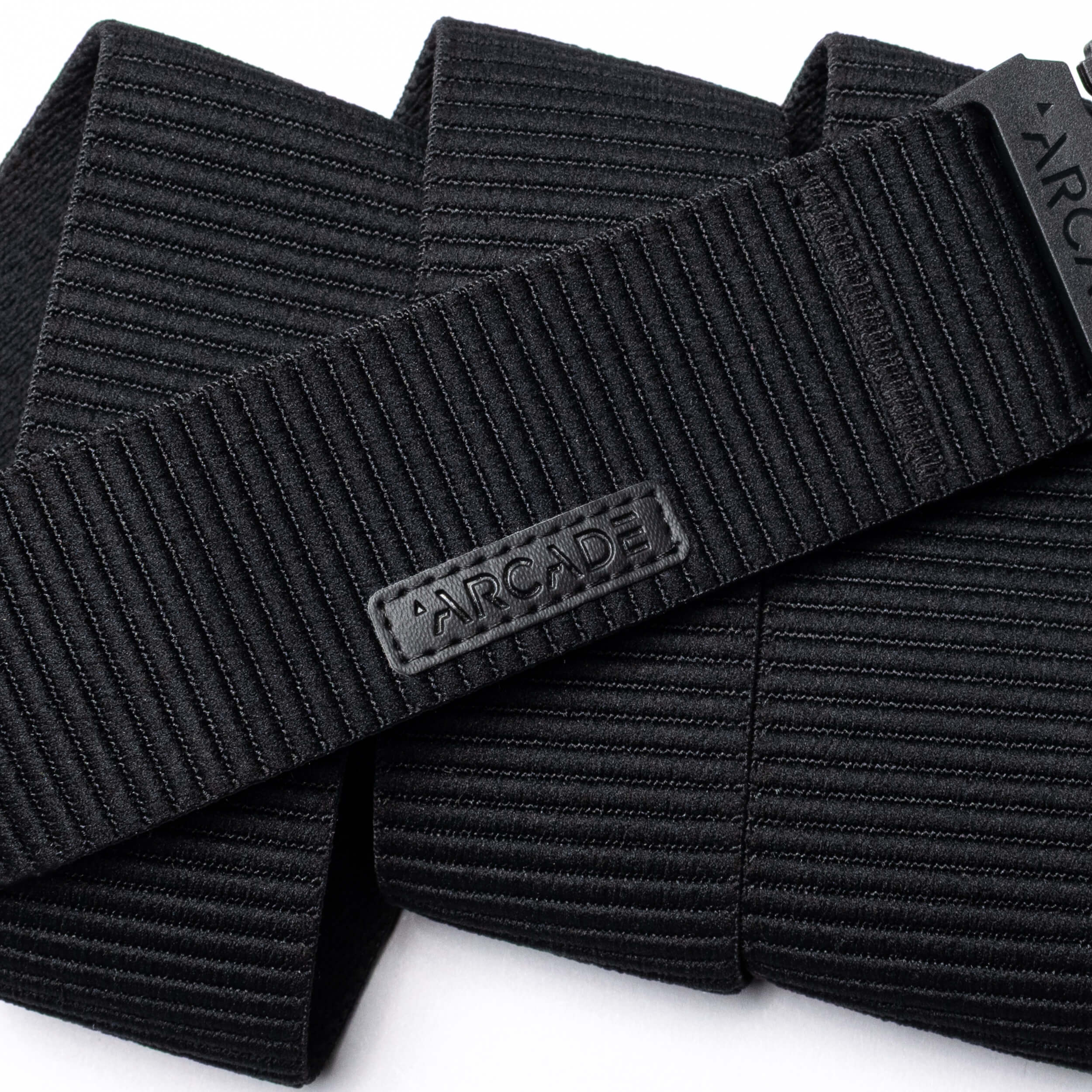 A close-up of the black, ribbed woven Woody belt by Arcade Belts features a rectangular patch with ARCADE in raised letters, showcasing its durable stitching and elastic stretch design.